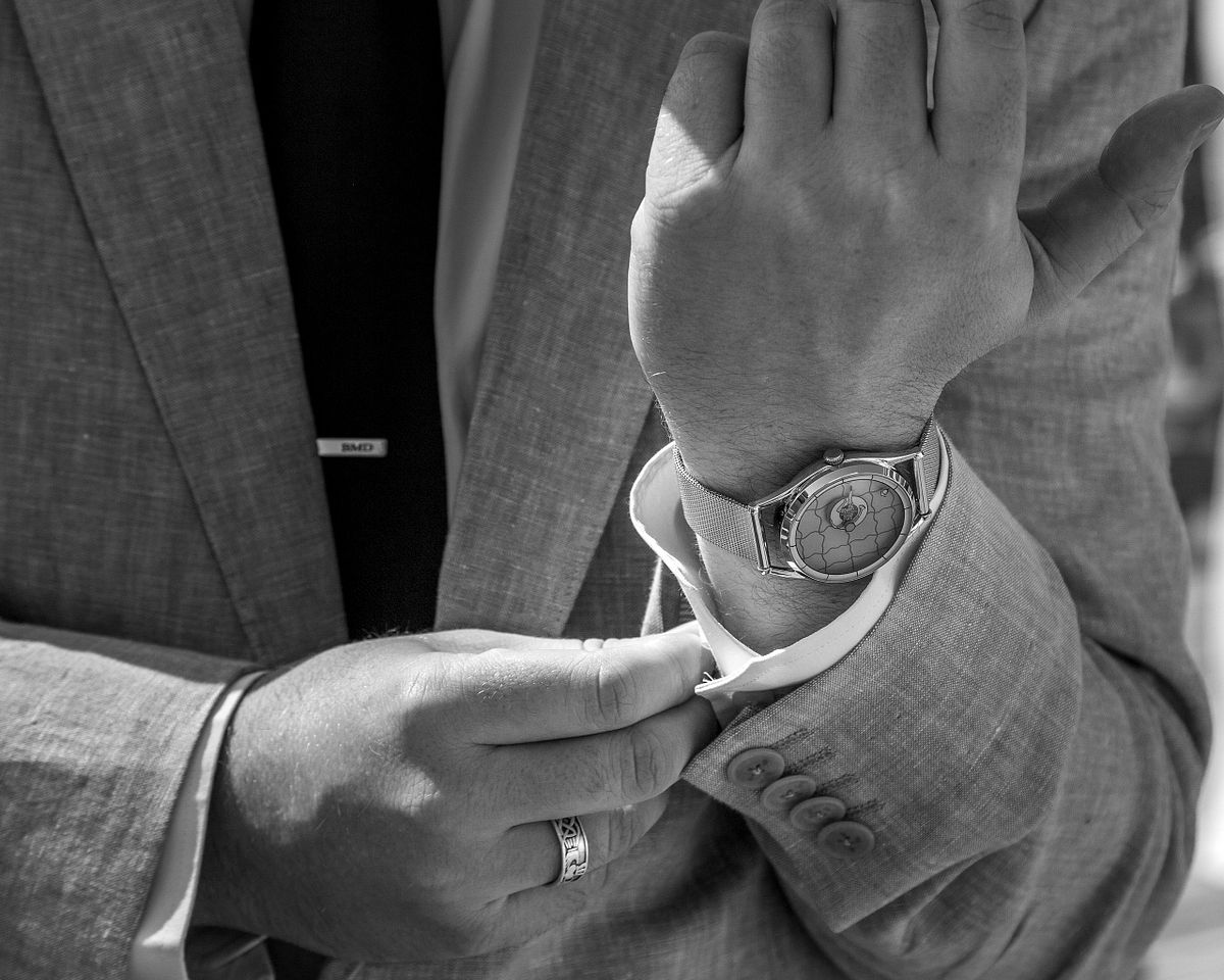 black and white photo of the groom closing the button of his shirt, his watch is showing