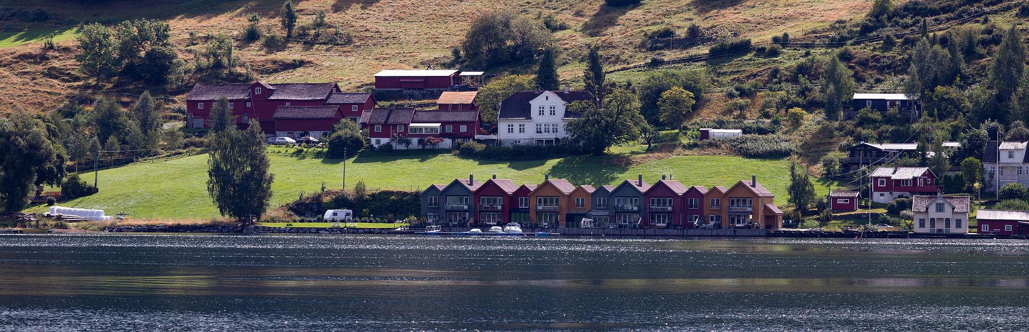 Hameau scandinave au bord de l’eau, reliefs en arrière-plan.
