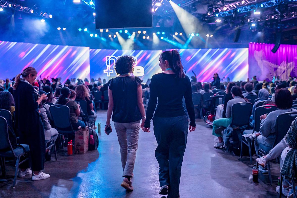 Corporate event photography capturing two attendees walking hand-in-hand toward the main stage at the Grace Hopper Celebration 2024 in Philadelphia, emphasizing inclusion, authentic connection, and representation within the tech community.