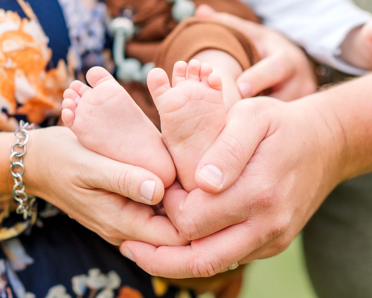 Husband and wife's hands holding their baby's feet