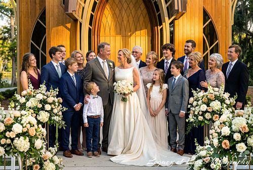 Large family and wedding party posing with a mature bride and groom inside a warm, golden-lit Florida chapel.