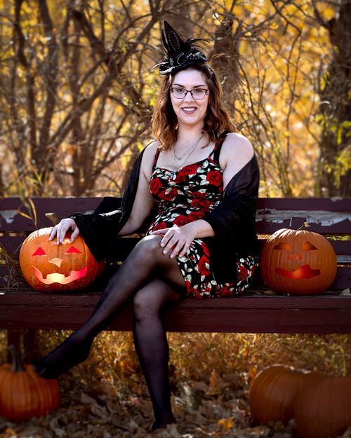 Energy crackles from a witch's finger tips while she sits on bench surrounded by jack-o-lanterns and pumpkins.