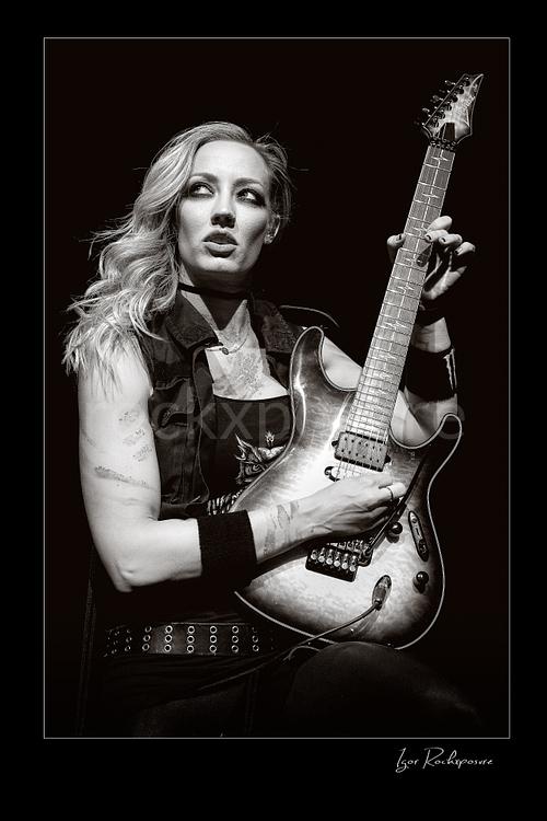 Vertical black and white image of Nita Strauss performing live on stage with an electric guitar in a close concert portrait