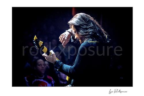 Horizontal color image of Michael Sweet of Stryper performing live with a black and yellow striped guitar in a dramatic stage portrait