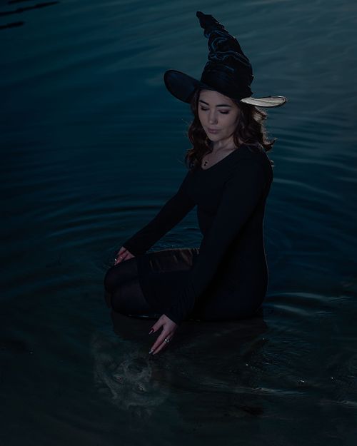 A witch looks at her wolfy reflection in the lake water.