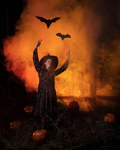 A witch sending bats off into the sky in a haze of orange light.