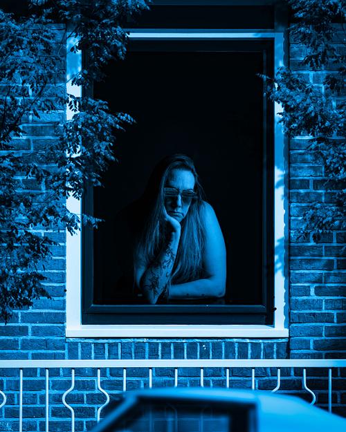 A blue scene of a woman wearing shades looking out the window a blue car.