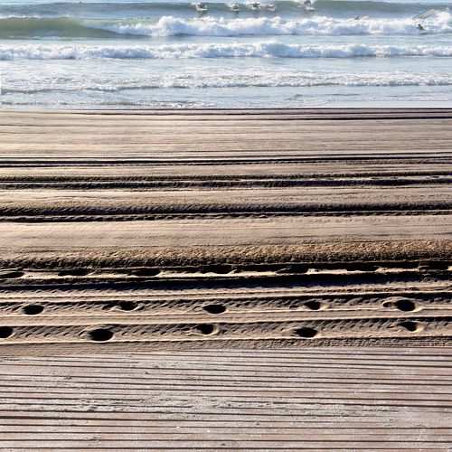 Beach lines in the sand, Footprints footp[rints, ocean waves, and surfers all aligned.