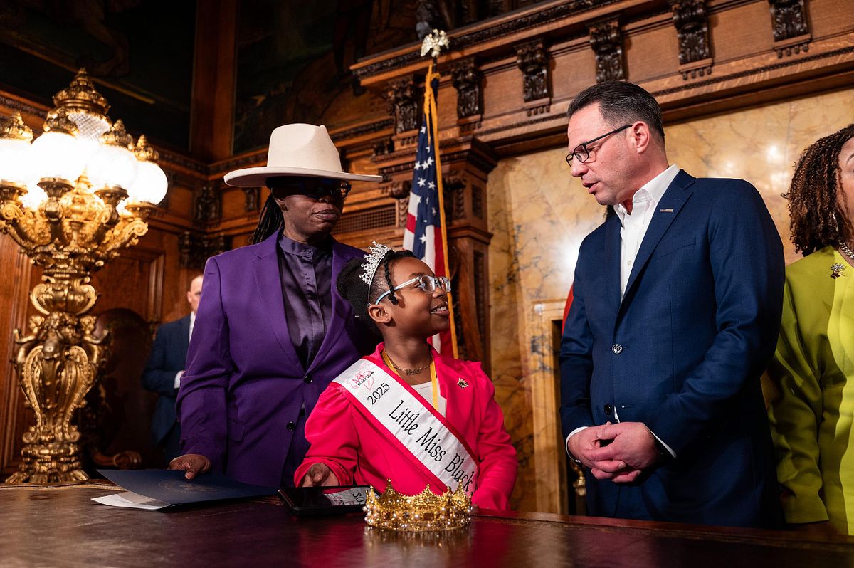 Governor Josh Shapiro speaks with Little Miss Black Pennsylvania during the CROWN Act signing in Harrisburg, capturing a candid moment of connection and representation in a historic leadership setting.