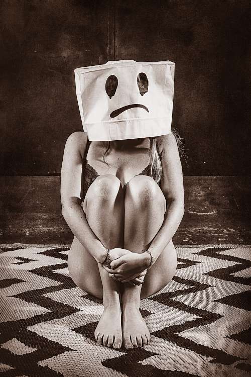 Femme assise au sol en lingerie avec un sac en papier sur la t&ecirc;te affichant un visage triste, illustrant l&rsquo;&eacute;puisement &eacute;motionnel et la solitude int&eacute;rieure malgr&eacute; une fa&ccedil;ade sociale