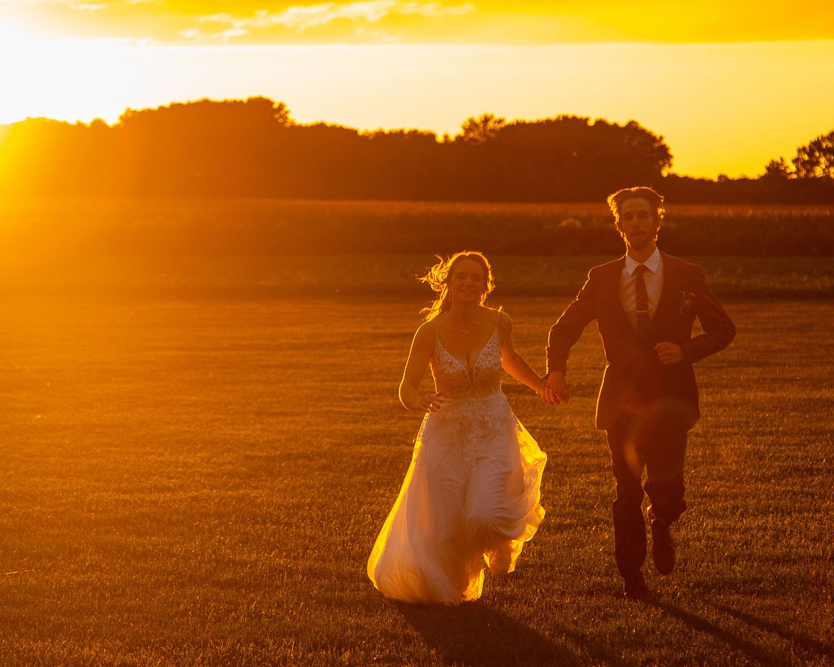 a just married couple running towards the camera as the sun is setting in the background on a hot summer's day