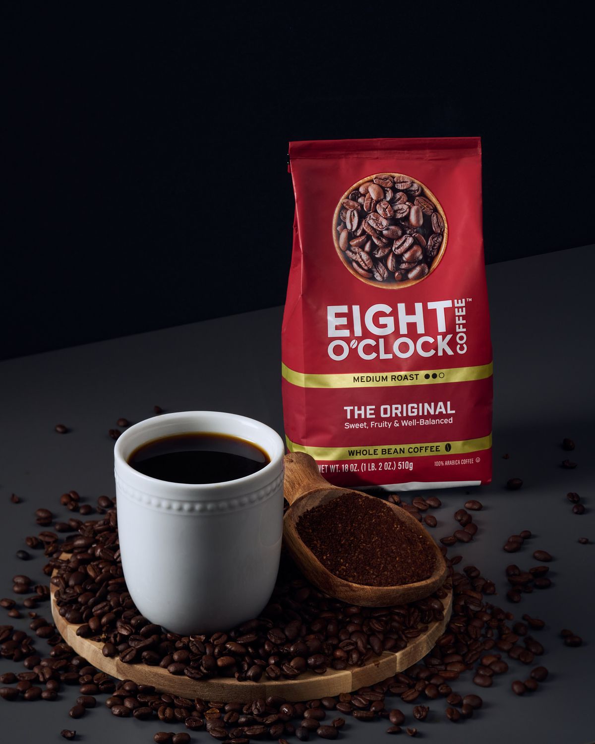 Coffee beans Spec Ad with a white ceramic cup of black coffee, coffee beans and ground coffee in a scoop.