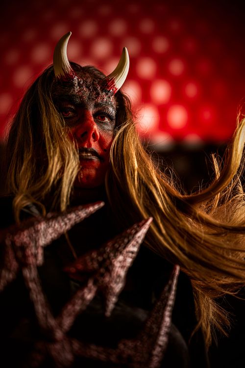 A devil in motion with a pitch fork agains a red and white dotted background.