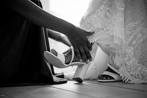 "dettaglio in bianco e nero delle mani di una damigella che mettono le scarpe alla sposa"