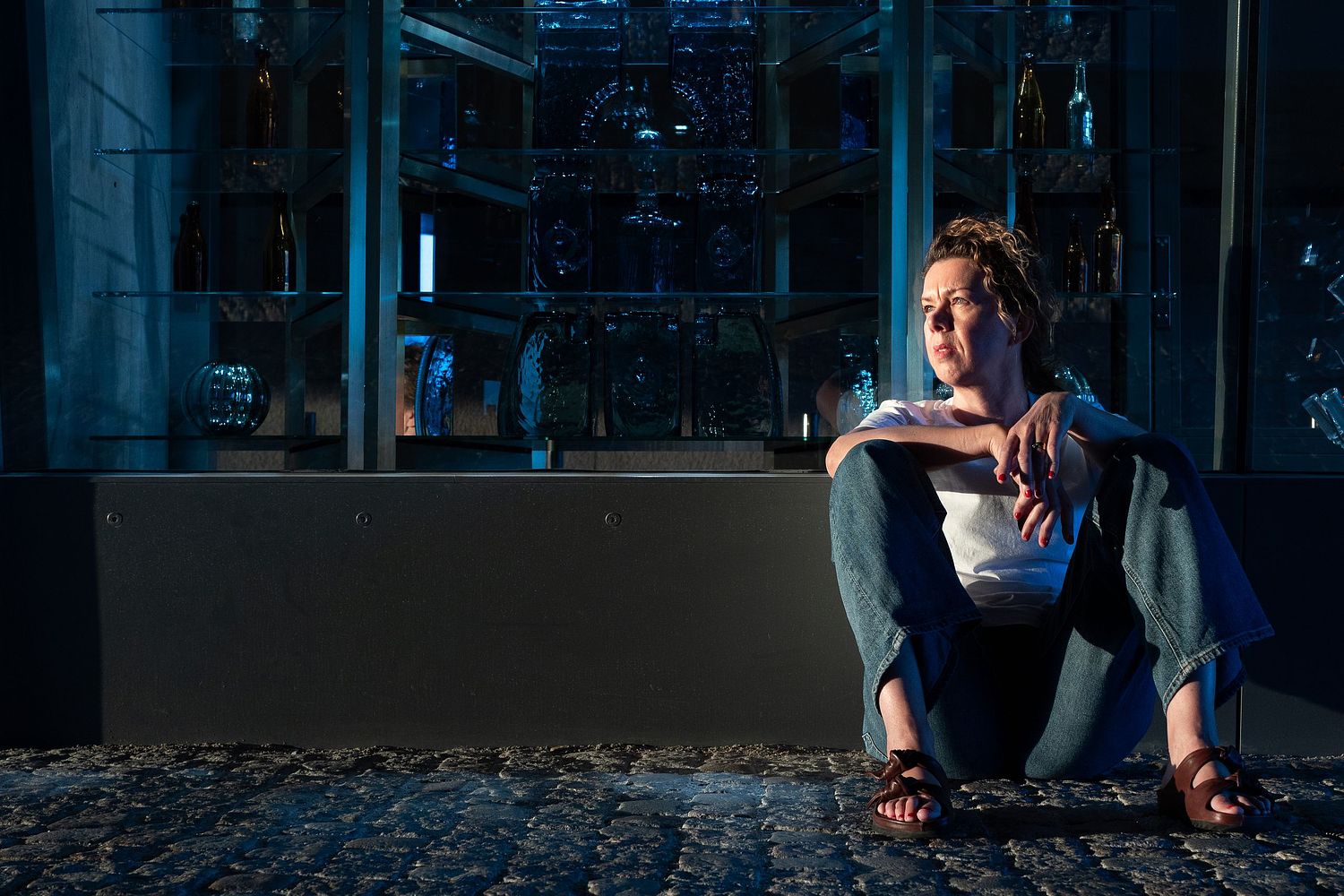 Editorial-style portrait of a woman sitting on cobblestone in blue-toned evening light, photographed in Stockholm by Mats Karlsson.