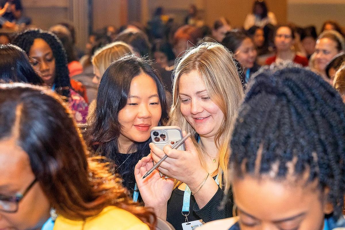 Corporate event photography capturing two attendees sharing a joyful moment during a session break at the Grace Hopper Celebration 2024 in Philadelphia, emphasizing authentic connection, representation, and community within the tech space.