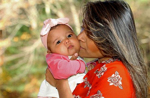 New mother kisses yound baby on her cheek