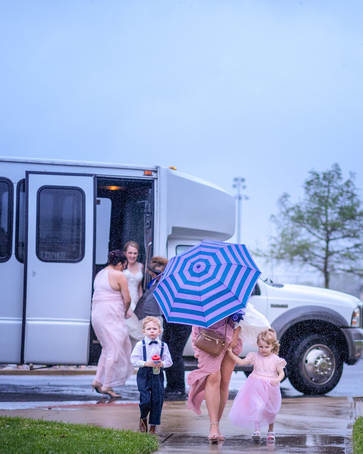 bride stepping of a bus during rain storm at Ross Station in Seaford, De. A bridesmaid is holding a  blue and white umbrella over her head
