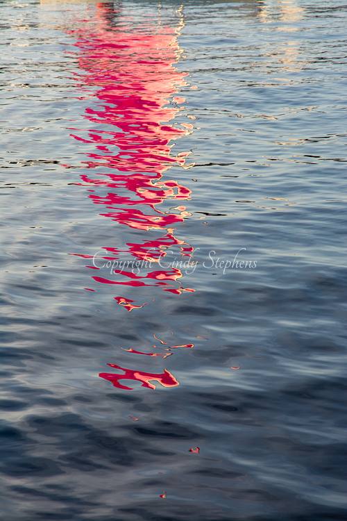 Reflection of a pink sailboat sail shimmering in the water at sunset