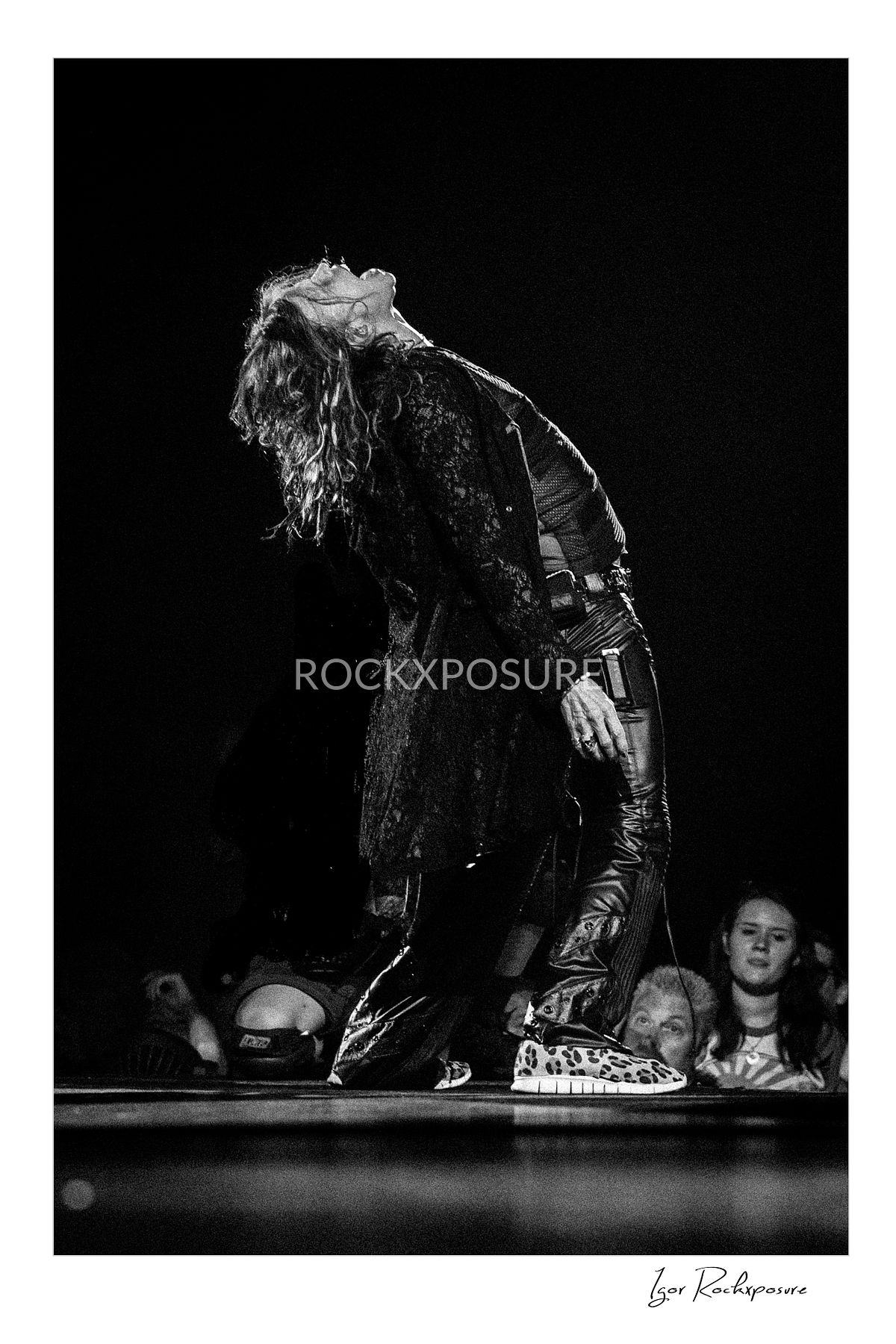 Vertical concert photography of Steven Tyler bending backward on stage in black and white photography under stage lighting