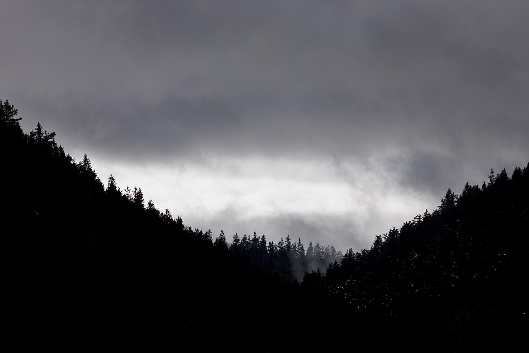 Dark mountain valley with central light opening through mist – atmospheric landscape photography