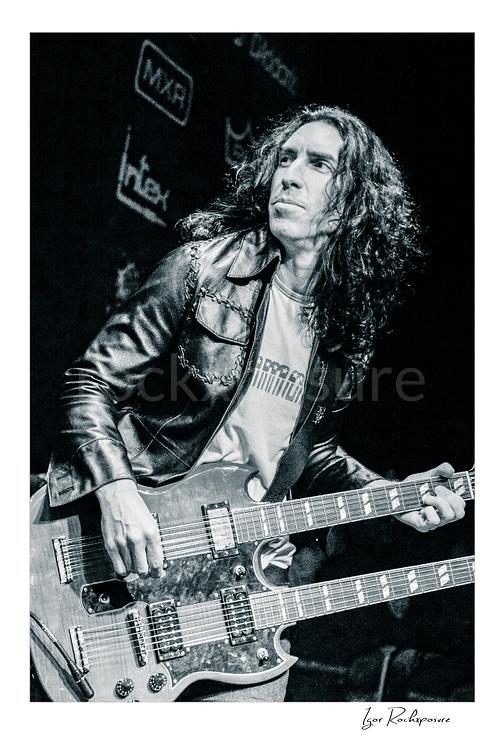 Vertical black and white image of Brent Woods playing double-neck guitar on stage in a tight performance shot
