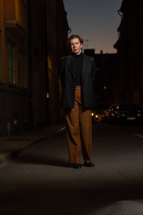 Helkroppsporträtt av kvinna i urban kvällsmiljö med stadssilhuett och gatljus i bakgrunden, Stockholm.