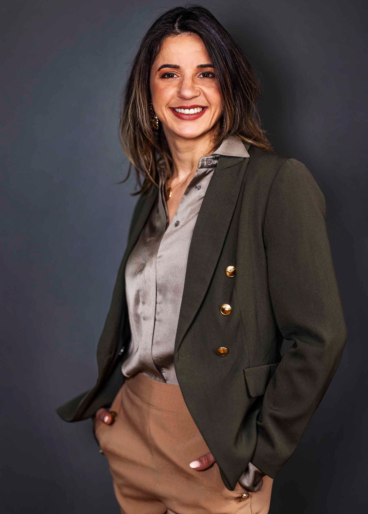 Corporate portrait of a female business woman wearing a brown pants, a dark suit, against a dark grey background.