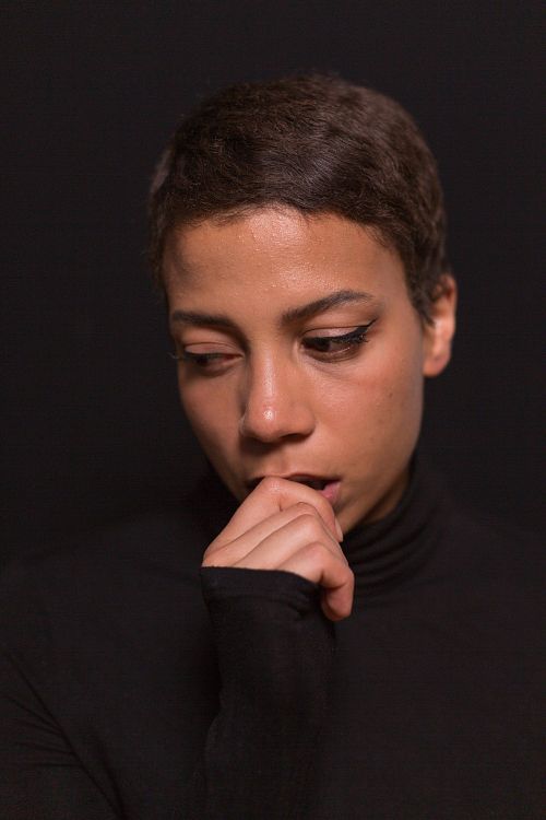 A headshot of a woman with a hand placed against her mouth, dressed in a black turtleneck.