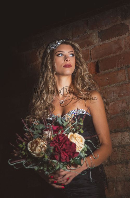 Model wearing a black wedding dress from Bridal Re-Loved Leicester, holding a beautiful bouquet against a brick wall backdrop, photographed by Weddings by Jermaine, with hair and makeup by Justaboutweddingshair and beauty, and accessories by Sydney Grace Bridal