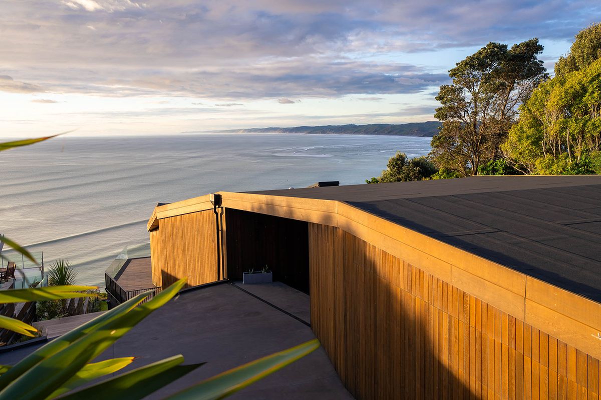 Exterior architectural photography of a modern timber-clad luxury home overlooking the ocean at sunset in Raglan.