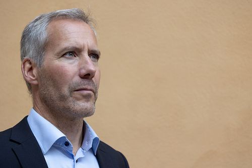 Professional business portrait of a man in a suit against a beige wall, photographed in Stockholm by Mats Karlsson.