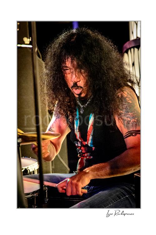 Vertical color image of Frankie Banali playing drums onstage in a tight live performance close-up with intense expression