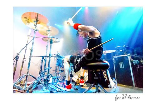 Horizontal color image of Zoltan Chaney playing drums under bright blue and purple stage lighting