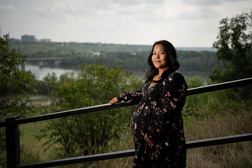 Expecting mother standing a railing with the river valley flowing behind her.
