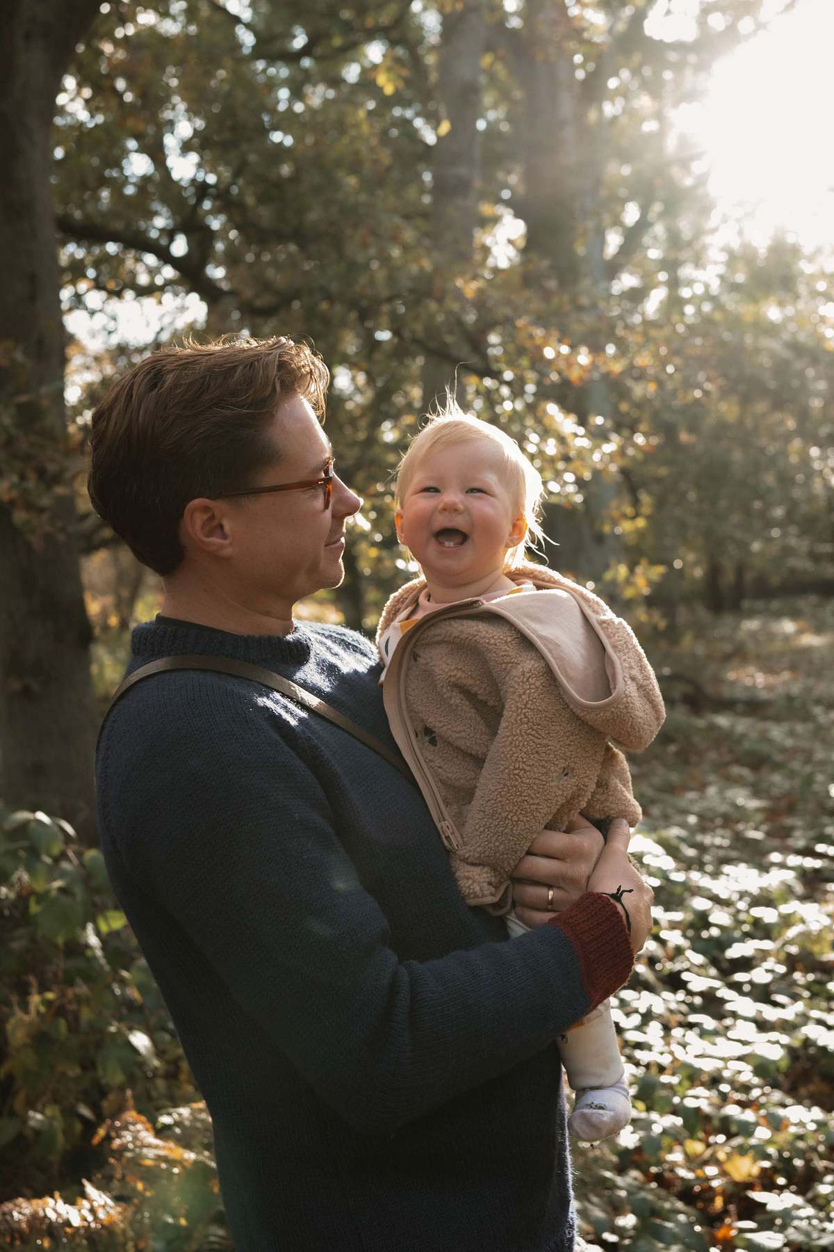 Father holding laughing baby outdoors in woodland, natural family lifestyle photography UK