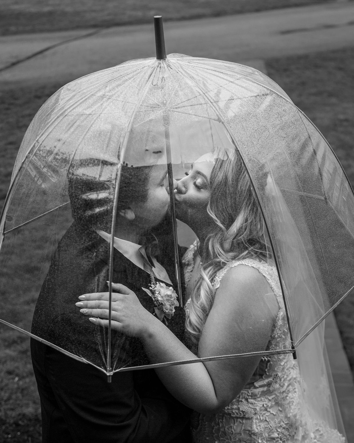 bride and groom kissing under an umbrella during a rain storm. the photo is black and white