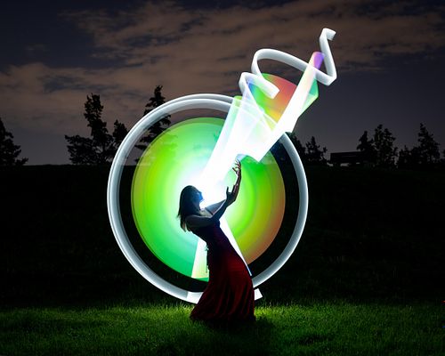 Grad photo of a young woman in a sphere of painted light sending ribbons of light to the sky.