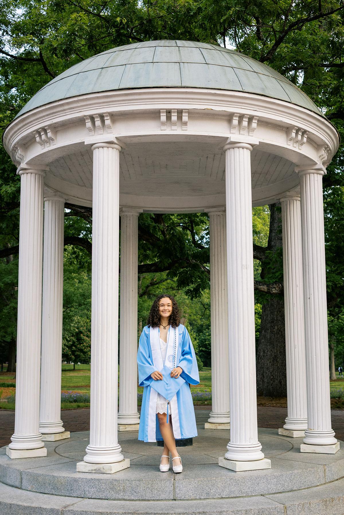 A woman in her graduation robe and stole at the Old Well on UNC's campus in Chapel Hill, NC