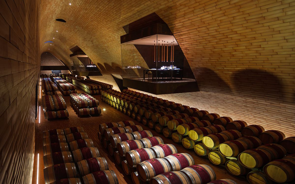 A dramatic perspective of the subterranean aging cellar at Antinori nel Chianti Classico featuring rows of oak barrels beneath rhythmic terracotta-tiled vaults and architectural glass viewing pods.