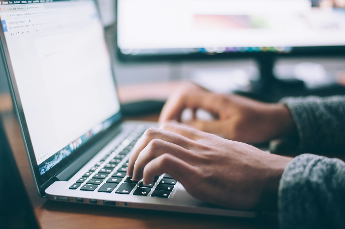 Person typing on a laptop keyboard with a monitor in the background