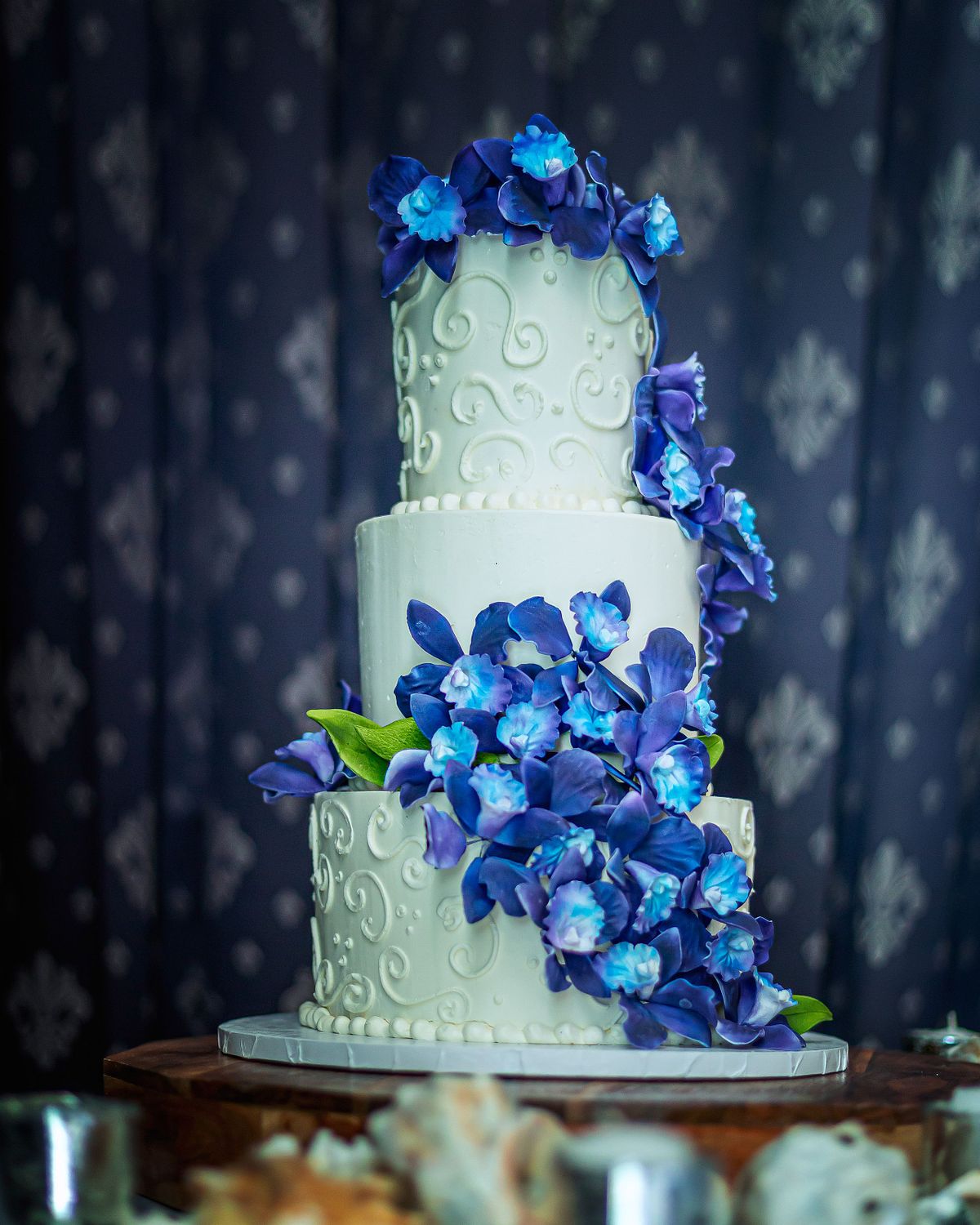 A three-tier white wedding cake decorated with vibrant blue orchids, captured with punchy editorial colors and high contrast.
