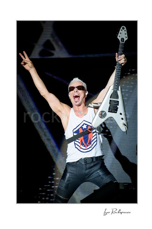 Vertical color image of Rudolf Schenker of Scorpions performing live with white guitar raised, sunglasses, and both arms lifted high