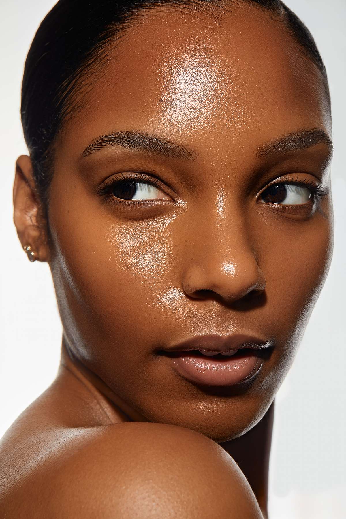 Close-up portrait of a woman with radiant, dewy dark skin looking back over her shoulder.
