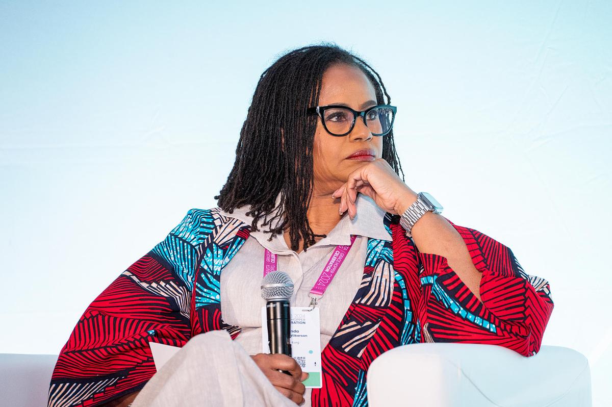 A keynote speaker sits thoughtfully on stage holding a microphone during a corporate leadership panel discussion at a professional conference.
