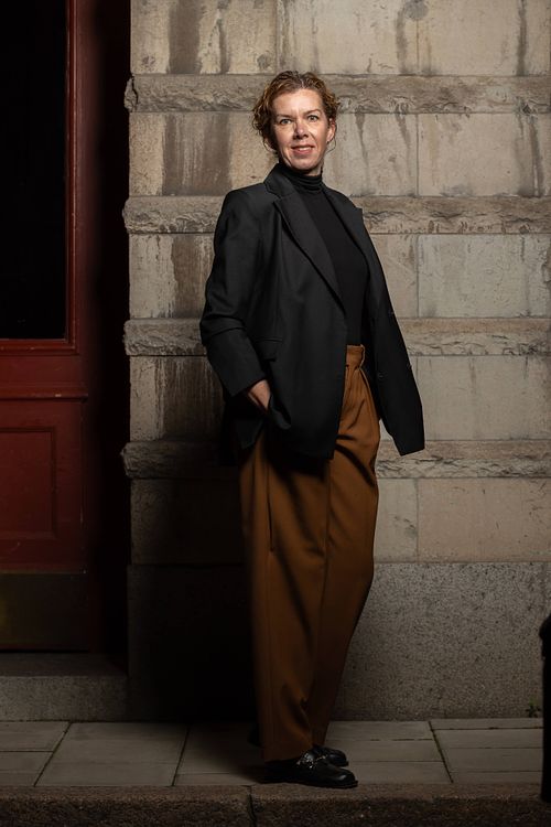 Helkroppsporträtt av kvinna i businessklädsel i stadsmiljö mot stenfasad, personal branding i Stockholm.