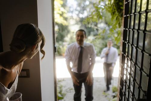 La sposa guarda verso l&rsquo;esterno mentre la luce entra dalla porta in controluce.