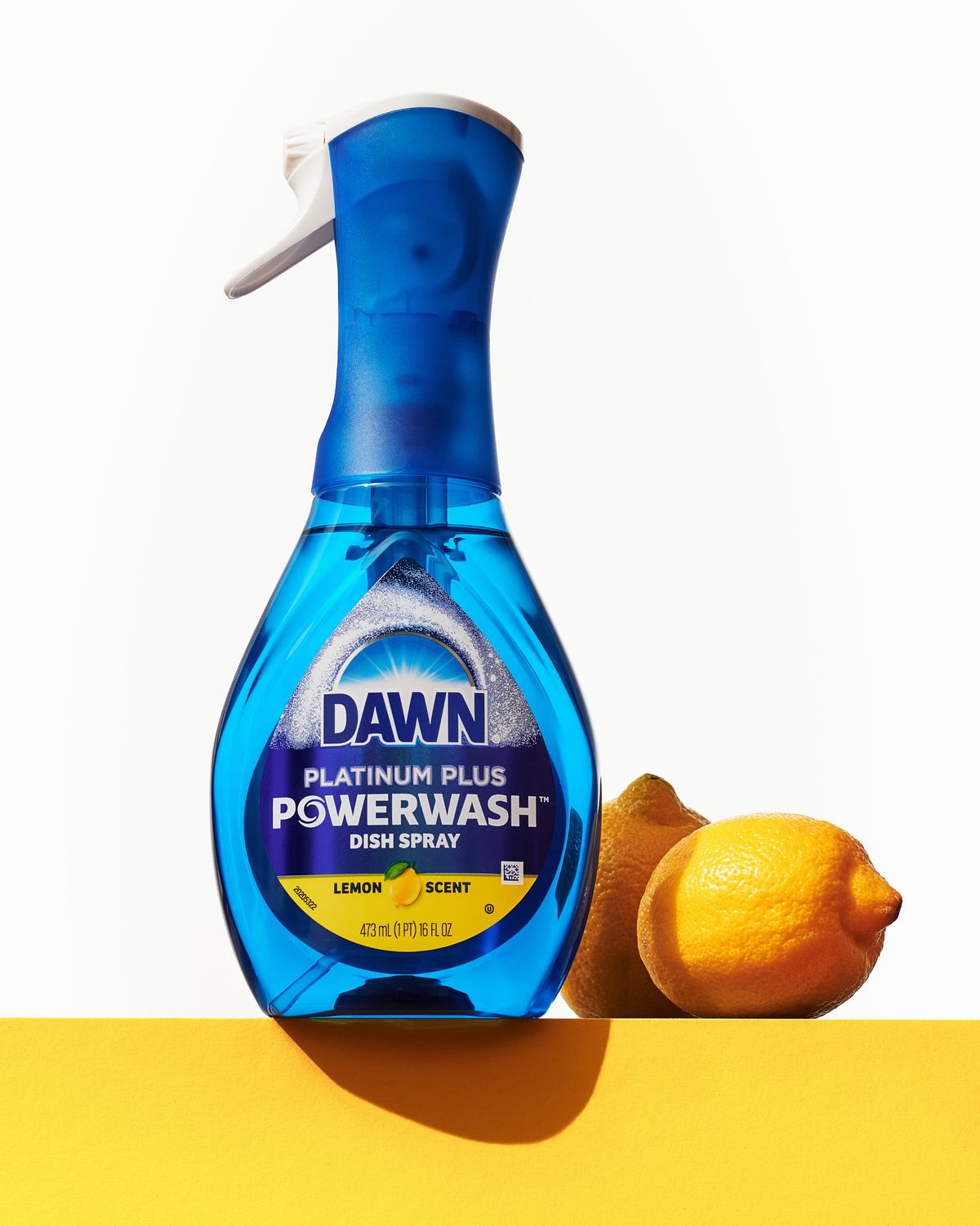 Brightly lit bottle of dish washing detergent beside two lemons.