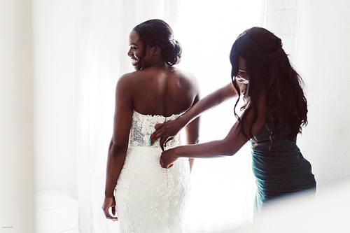 "damigella che allaccia vestito alla sposa di spalle"