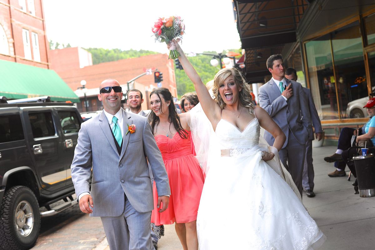 Bride lifts her bouquet in the air as her wedding party walks behind her